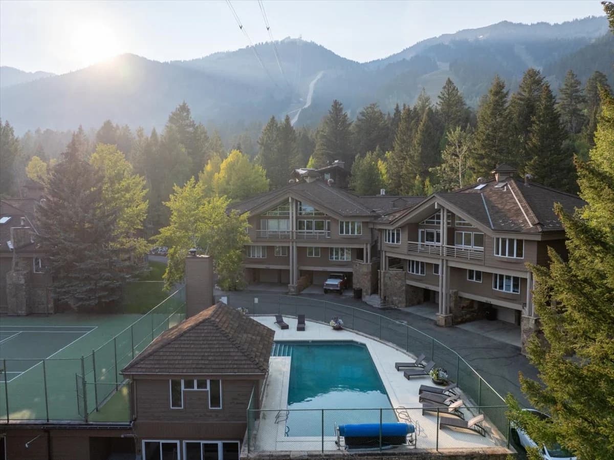 Aerial view of condo complex with pool, tennis court, and ski resort backdrop